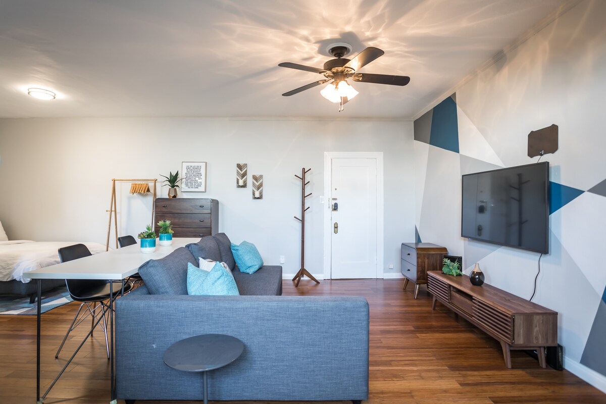 La moderna sala de estar de tamaño modesto cuenta con una llamativa pared pintada geométrica y un diseño interior elegante pero funcional. ¿Listo para relajarte y recargar energías? ✨