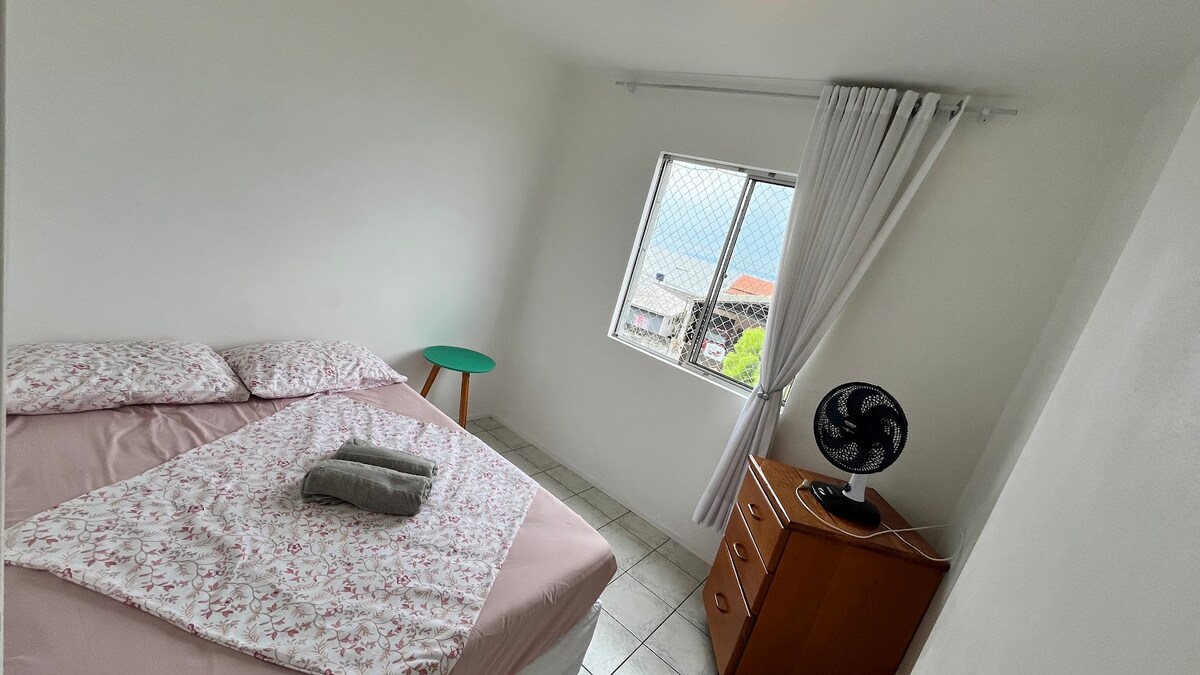 חדר שינה עם מיטה זוגית, שידה, שידה ליד המיטה ומאוורר.