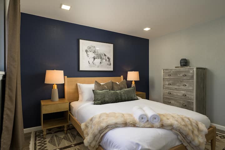 Elegante dormitorio con una lujosa cama tamaño queen, pared decorada en azul marino, iluminación cálida y texturas acogedoras. Un refugio relajante diseñado para la comodidad y una gran noche de sueño.