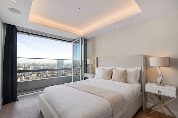 Chumba kikuu cha kulala chenye nafasi kubwa na kitanda cha ukubwa wa king, mashuka laini na madirisha makubwa yanayotoa mandhari mazuri ya jiji kwa ajili ya kukaa kwa utulivu na starehe.