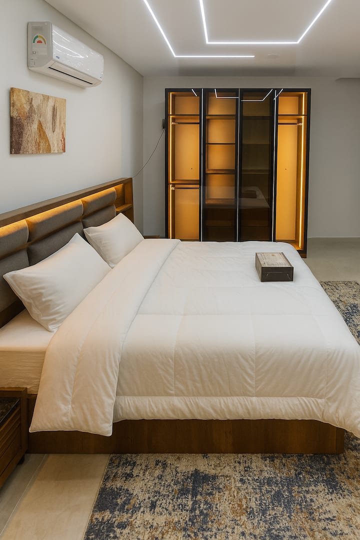 Chambre moderne et confortable avec un lit moelleux avec des draps blancs impeccables, des oreillers moelleux et une couette chaude. Un éclairage élégant et une armoire en verre élégante ajoutent une touche luxueuse. Propre, apaisant et parfait pour des nuits reposantes avec style.
