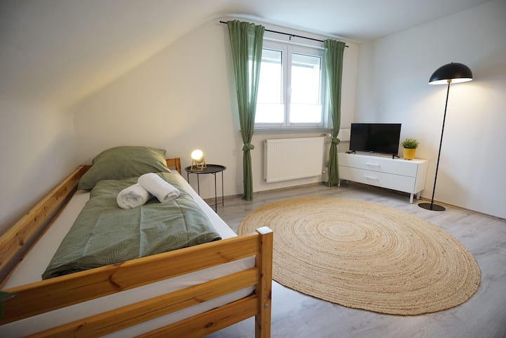Cama individual (90 x 200 cm) con ropa de cama básica y toallas. Las ventanas están equipadas con persianas plisadas, cortinas y persianas.