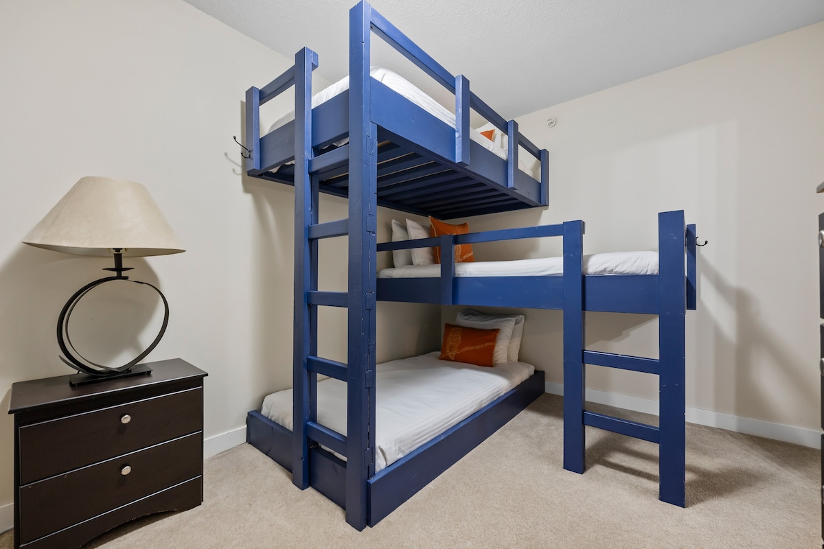 Troisième chambre/salle de séjour avec 4 lits simples, une commode et une télévision intelligente.