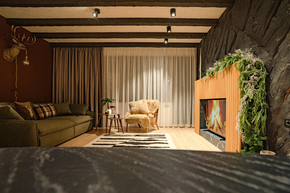 Sfeervol avondzicht op de woonkamer met open haard, zachte verlichting en gelaagde texturen. Een verfijnde alpenretraite waar comfort, warmte en ingetogen luxe moeiteloos samenkomen.