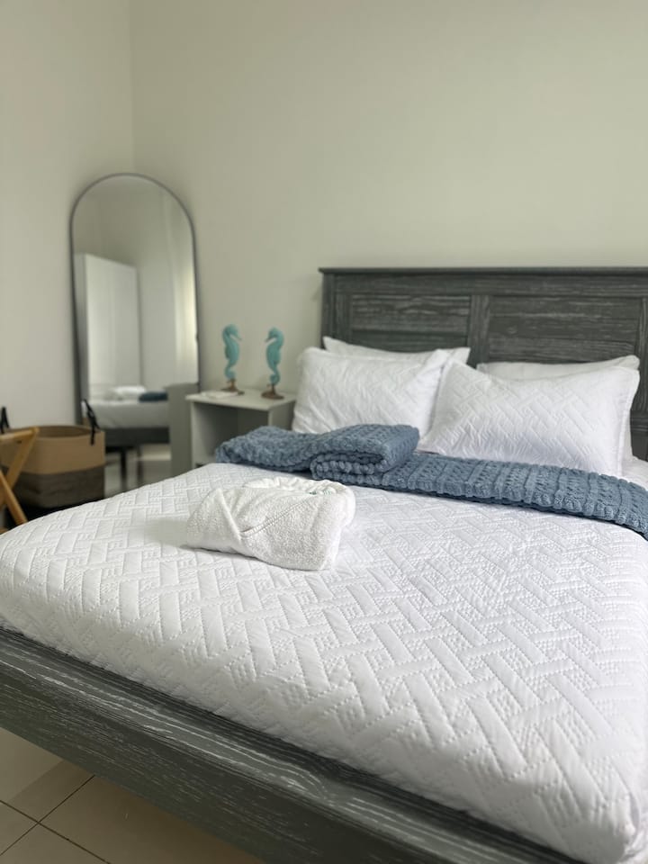 Chambre à coucher confortable avec un couvre-lit texturé, des draps doux et des tons neutres apaisants. Un miroir pleine longueur et des touches décoratives subtiles ajoutent de la chaleur, créant ainsi un espace détendu pour des nuits reposantes.
