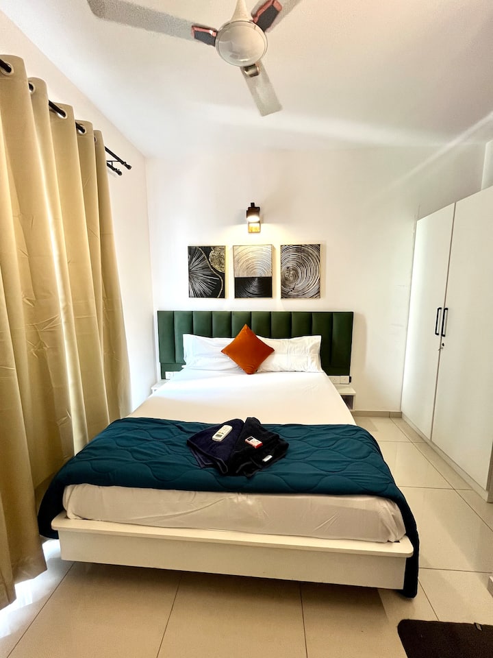 Duerme cómodamente en un dormitorio sereno con cama tamaño queen, sábanas frescas, aire acondicionado, ventilador, lámpara de noche y un armario para guardar tus artículos esenciales, perfecto para una estancia relajante.