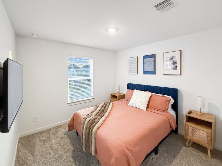 Inviting secondary bedroom with a cozy bed, soft carpeting, and a wall-mounted TV. Styled with warm tones and simple décor for a restful stay.