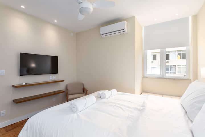 Habitación amplia e iluminada con aire acondicionado, TV, persianas y silla. /Amplio dormitorio luminoso con aire acondicionado, TV, persianas y silla