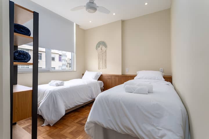  Dormitorio con 2 camas, ventilador de techo, persiana y estantería. / Dormitorio con 2 camas individuales, ventilador de techo, persianas y estantería. / Habitación con 2 camas, ventilador de techo, persianas y estante.