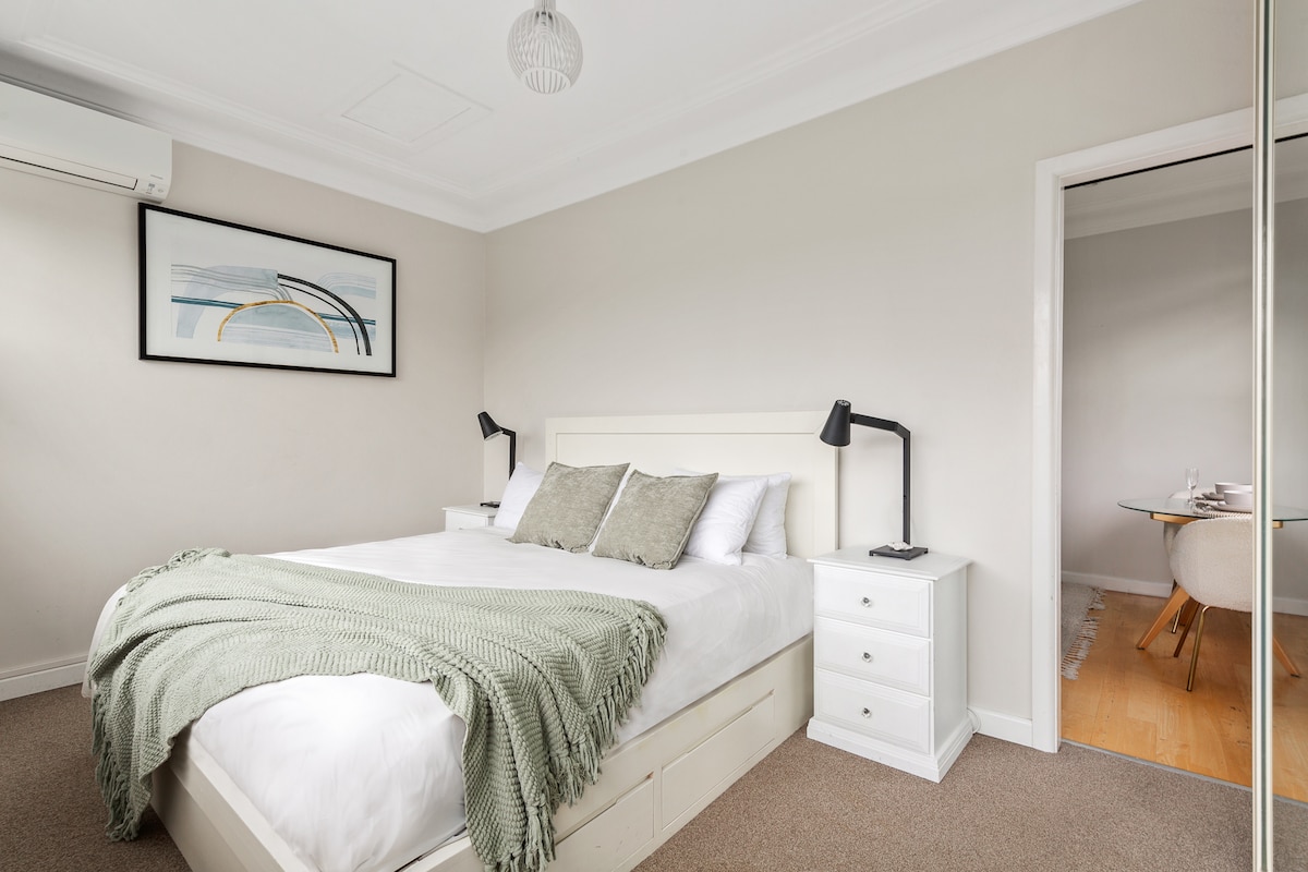 El tranquilo dormitorio ofrece una cama tamaño king con ropa de cama de calidad, persianas opacas, un armario empotrado con espejo, aire acondicionado de sistema dividido y una vista frondosa elevada.