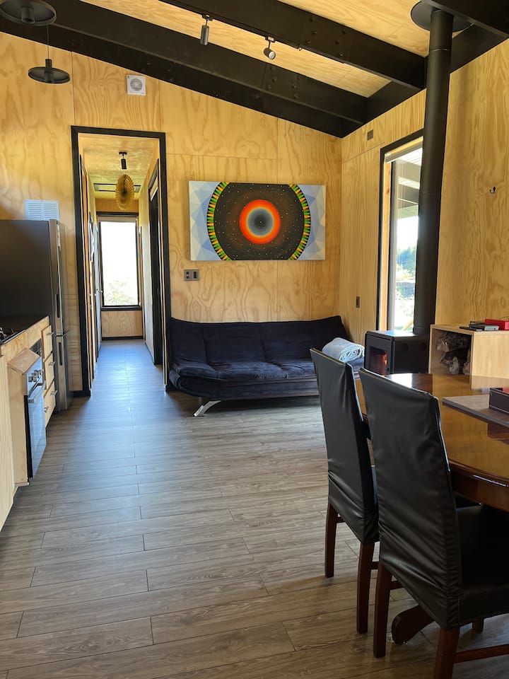 Сърцето на дървената колиба е интериорът, където можете да се насладите на времето си, споделяйки масата за хранене или почивайки на разтегателния диван с изглед към реката и гората, отоплявани с печка на дърва. Имате също и смарт телевизор, Bluetooth високоговорител, карти за игра. 