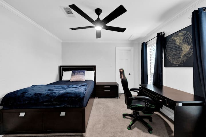 Bedroom perfect for gamers and remote workers, featuring a spacious dark wood desk, and a cozy bed.