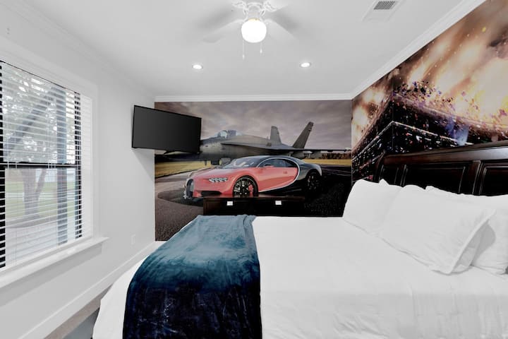 Action-packed themed bedroom, boasting a dynamic sports car and fighter jet mural, a grand dark wood bed, and a wall-mounted TV.