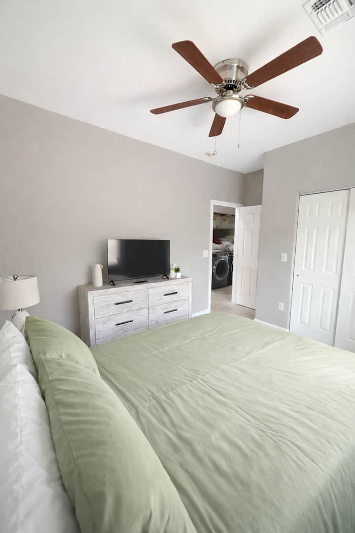 Dormitorio luminoso y cómodo con una cama acogedora, sábanas suaves, mesita de noche, vestidor y televisor. La luz natural inunda la habitación, y el ventilador de techo mantiene el espacio fresco y cómodo. Perfecto para relajarse después de un largo día.