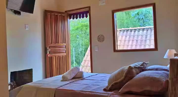 Habitación con vista a la naturaleza, cama doble equipada, Smart TV, chimenea interna, ropa de cama y minibar.