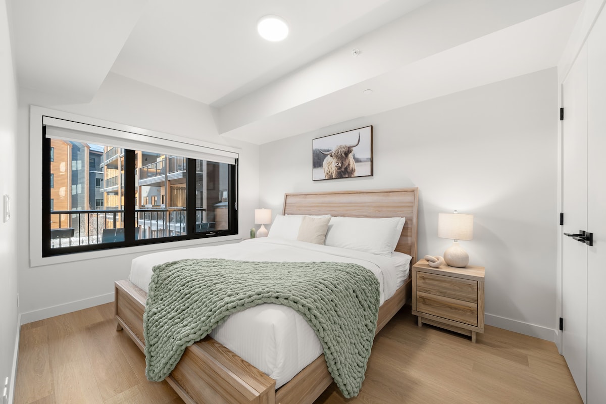 明亮的卧室，配有温暖的木质饰面、床头柜和温馨的布局。