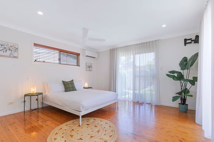 El dormitorio principal cuenta con una cama tamaño queen, estilo costero suave y acceso directo a la terraza junto a la piscina, junto con aire acondicionado de sistema dividido y un baño privado para una comodidad relajada y privada.