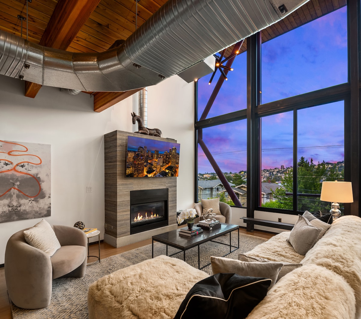 A spacious living area features light wooden flooring, with a large white sofa positioned in front of a television unit. A modern dining table and chairs are visible in the background, along with a well-equipped kitchen that includes built-in appliances.