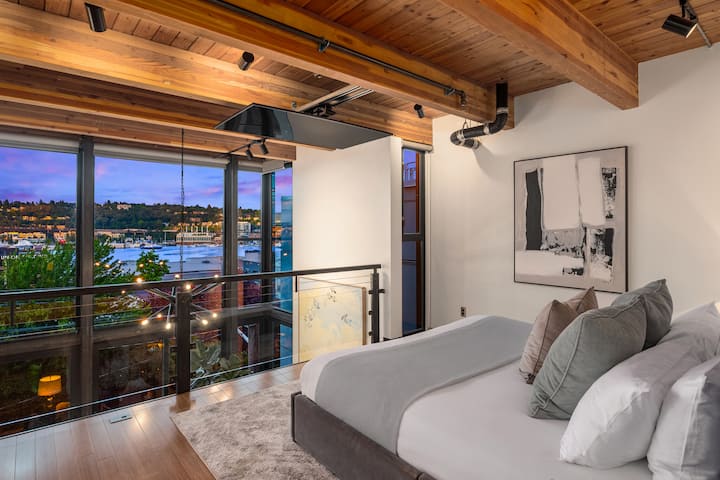 Spavaća soba s bračnim krevetom (king size) i pogledom na dnevni boravak i jezero South Lake Union iz kreveta. Probudite se uz zoru, opustite se uz TV koji se spušta za filmske večeri i uživajte u prozračnom, otvorenom potkrovlju ispod toplih drvenih greda.