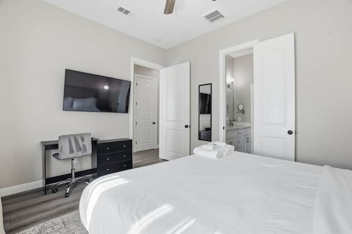 Spacious king bedroom with a private ensuite bath, mounted TV, and work desk—combining comfort, privacy, and convenience.