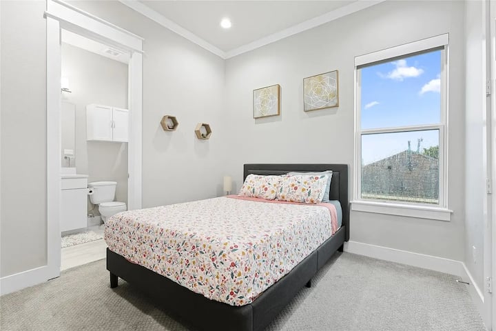 Comfortable queen bedroom featuring electric shades, a TV, and a private en-suite bathroom for added privacy and convenience.