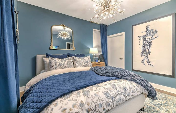 Elegant bedroom with bold blue décor, plush bedding, statement chandelier, stylish artwork, and cozy lighting—creating a luxurious and relaxing retreat.