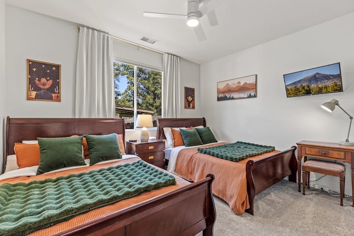 The ground-floor guest bedroom features two queen beds, blackout curtains for a perfect night's sleep, and a charming workspace crafted from a vintage sewing table. Enjoy forest views and a smart TV.