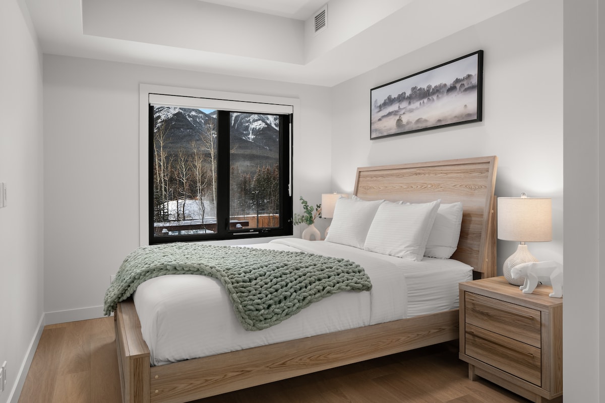 Svetlá a upokojujúca spálňa č. 1 s manželskou posteľou, kvalitnou posteľnou bielizňou, osvetlením pri posteli a výhľadom na hory cez veľké okná.