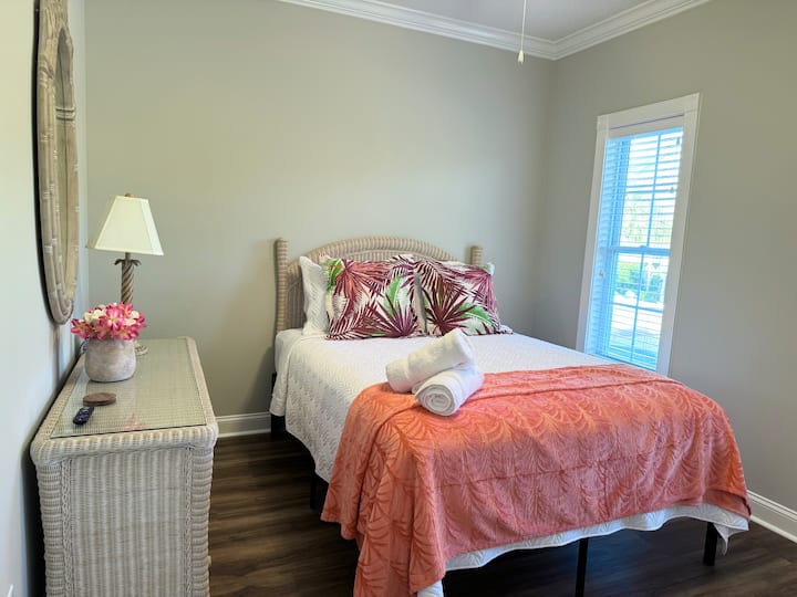 Spavaća soba s bračnim krevetom (širine 150 – 179 cm) uređena u živopisnim bojama.  Pametni televizor. Pogled na tropsko dvorište.