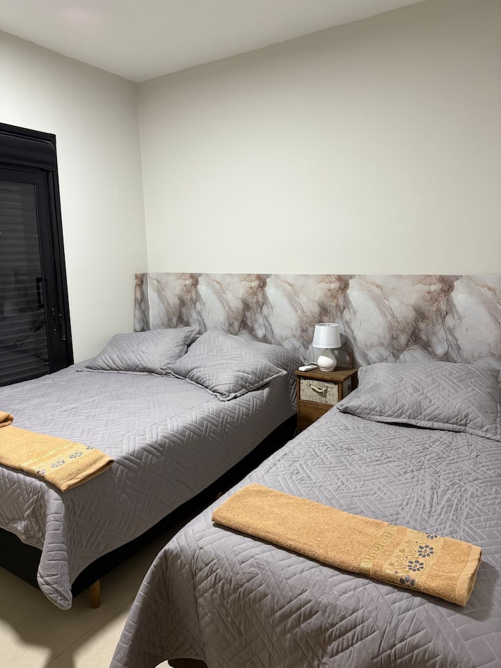 Habitación delantera con balcón y persianas opacas. 
1 cama matrimonial 
1 cama individual 
1 mesita de noche con lámpara 
2 aparadores para maletas y bolsas 
1 alfombra