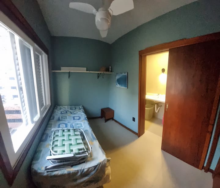 Dormitorio con cama individual, ventilador de techo y baño privado.
Se puede ver el océano desde la ventana.