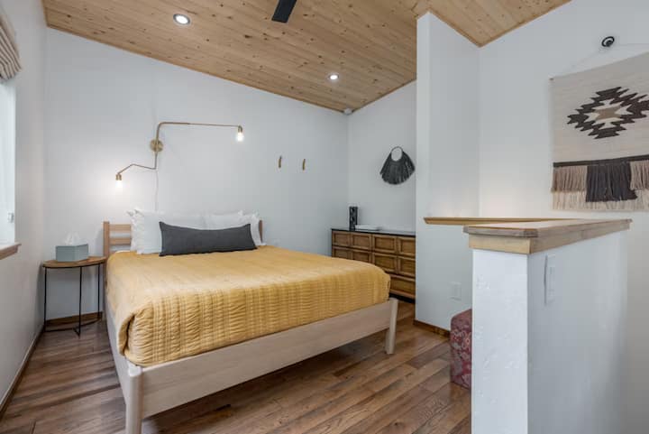 Bright queen bedroom with wood ceilings and blackout window coverings.