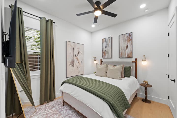 Dormitorio tamaño queen con arte mural de galería, apliques junto a la cama, cortinas opacas y TV Roku: cada dormitorio es un refugio en sí mismo