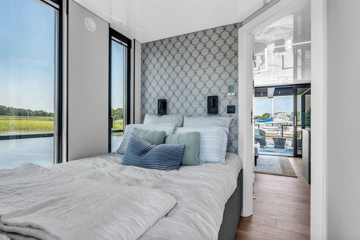 Serene, modern bedroom with a cozy bed, crisp linens, and elegant wall accents. Waterfront windows bring in natural light and calming lake views, creating a peaceful retreat perfect for restful nights on the water.