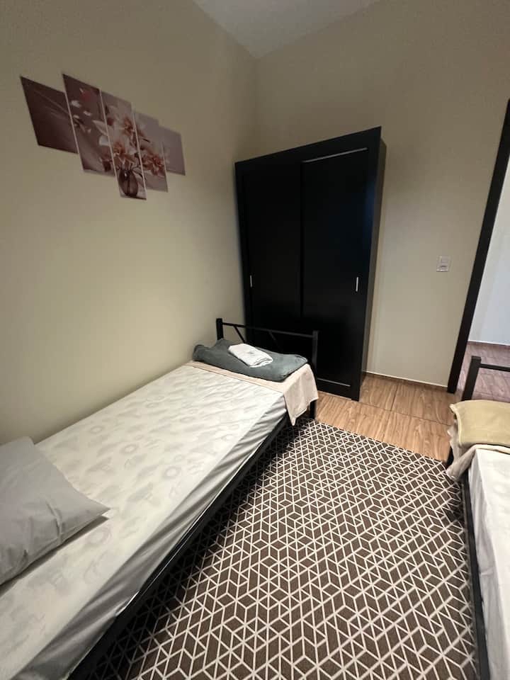 Dhomë komode dhe funksionale, ideale për të pushuar pas një dite pune ose udhëtimi. Hapësirë e pastër, e organizuar dhe e rehatshme me krevate tekë, ndriçim të këndshëm dhe perde errësuese për më shumë privatësi dhe qetësi.