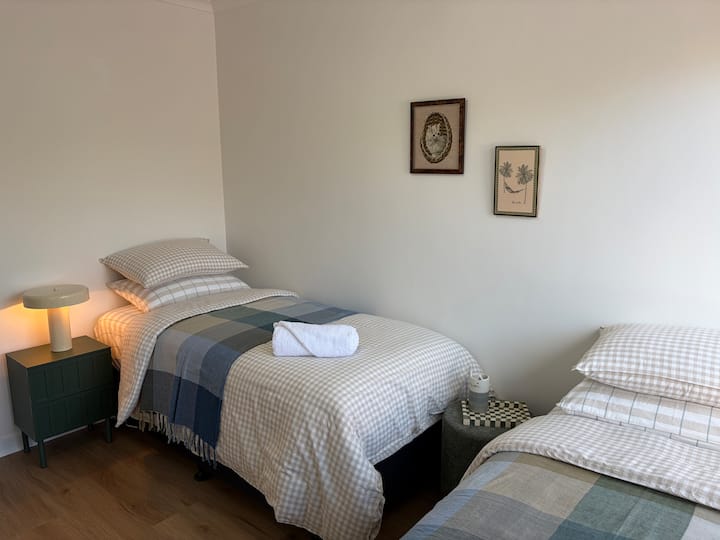 Una habitación doble luminosa con dos camas individuales, ropa de cama de calidad, un ventilador de techo para mayor comodidad y un armario empotrado con espejo para guardar cosas.
