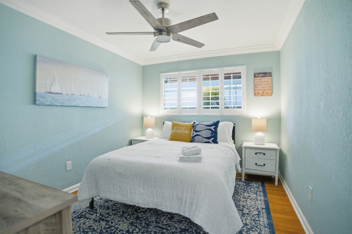 Retreat to this tranquil coastal bedroom featuring soothing blue walls, nautical-inspired artwork, and a plush bed perfect for a restful night.