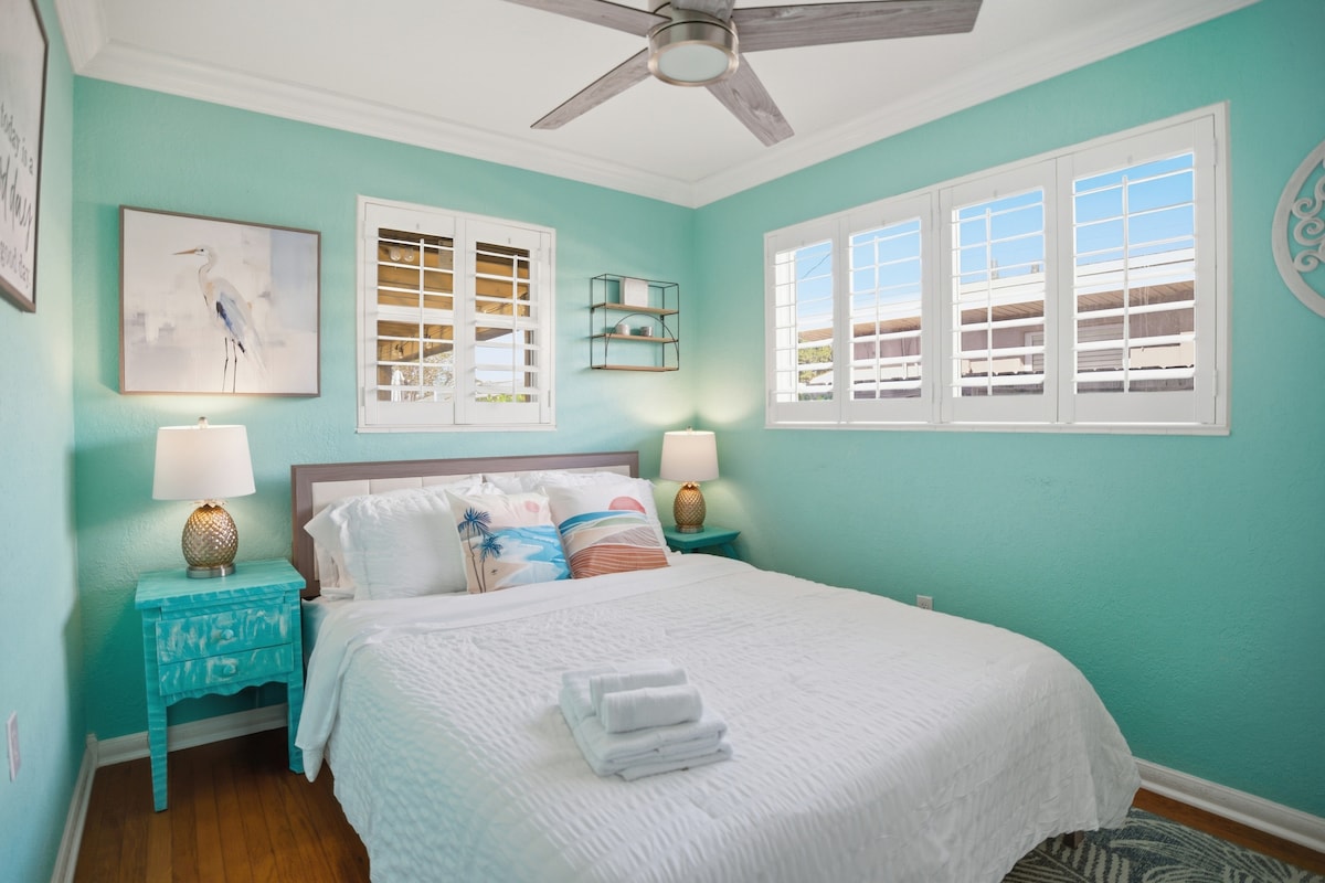 Unwind in this vibrant, sun-drenched guest room featuring tropical accents, elegant plantation shutters, and a cozy bed for a peaceful night's rest.