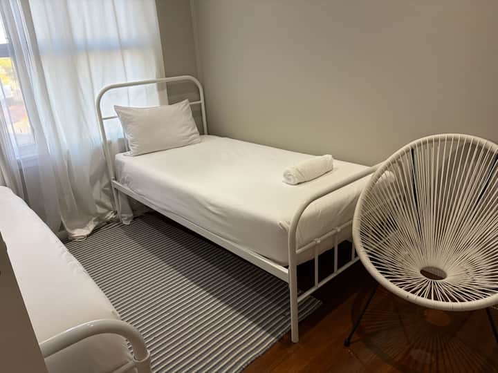 2nd bedroom with two single beds, air conditioning, and a ceiling fan. The east-facing window captures the morning sun