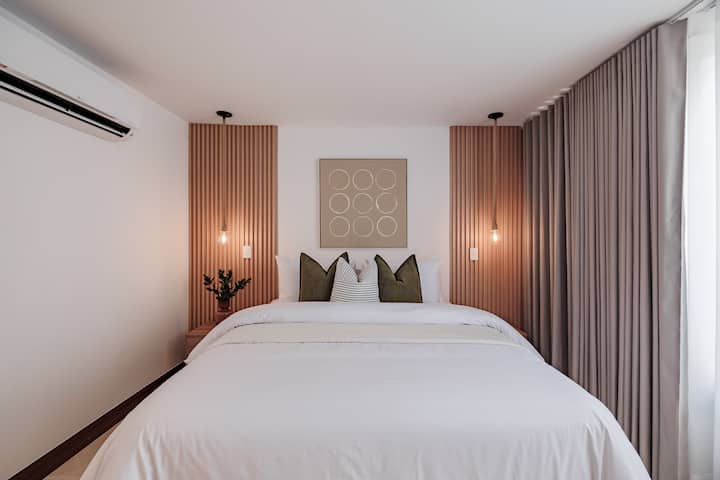 Suite privada #8: serenidad moderna. Un refugio elegante con una cama tamaño queen enmarcada por elegantes listones de madera e iluminación de estilo industrial. Una mezcla perfecta de texturas orgánicas y diseño limpio para una estadía tranquila.