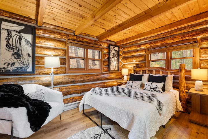 Comfortabele hoofdslaapkamer met een queensize bed, houten muren en een warme hutinrichting.