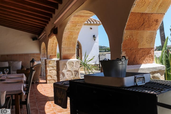 Terraza cubierta con barbacoa y zona de comedor bajo los arcos: el rincón perfecto para las parrilladas.