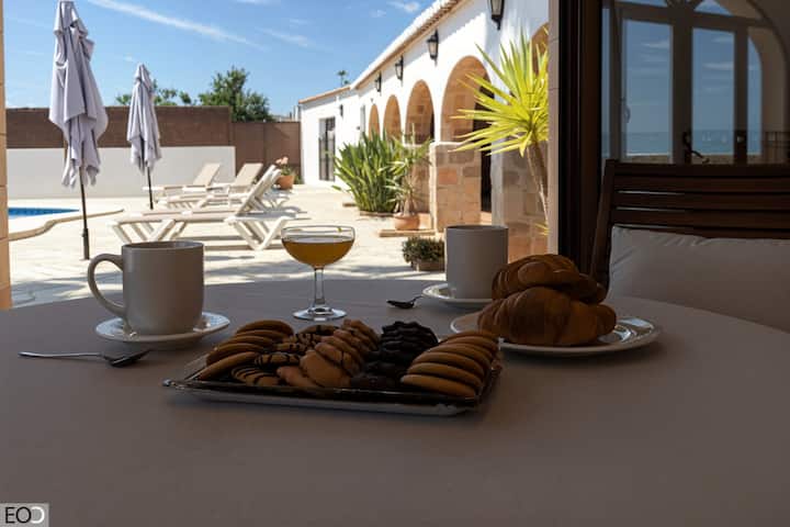 Mesa del comedor exterior con desayuno servido y la piscina al fondo: mañanas de villa.