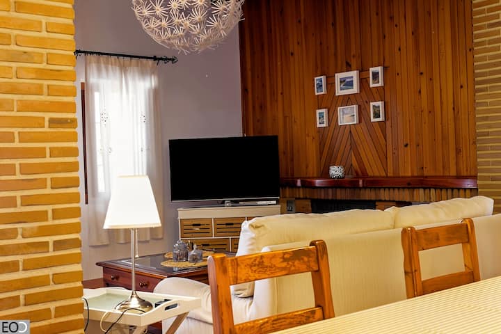 Salón con TV, pared de madera y sofás claros: ambiente cálido y confortable.
