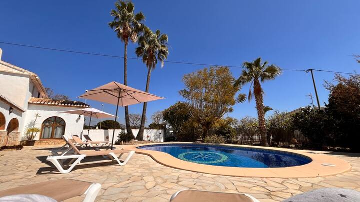 Piscina con zona de tumbonas y sombrilla entre palmeras: descanso al aire libre.