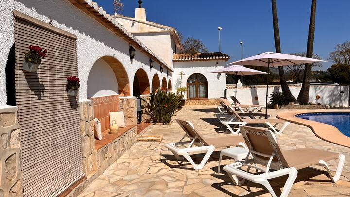 Piscina con tumbonas y la fachada de arcos de la villa: relax total al aire libre.