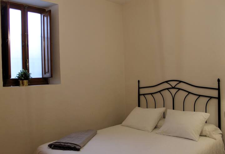 Dormitorio 2 con cama de matrimonio y cabecero de forja junto a la ventana: descanso tranquilo.