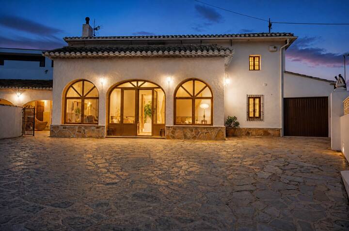 La villa iluminada al anochecer, con sus ventanales en arco: acogedora y con mucha personalidad.