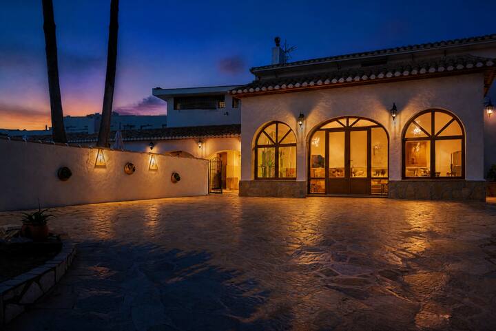 Fachada de la villa iluminada al atardecer, con amplio patio: estampa espectacular al caer la tarde.