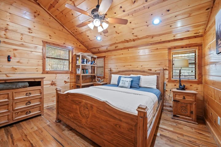 Wood-clad bedroom with cozy bed, bookshelf, and “Life is good” pillow.